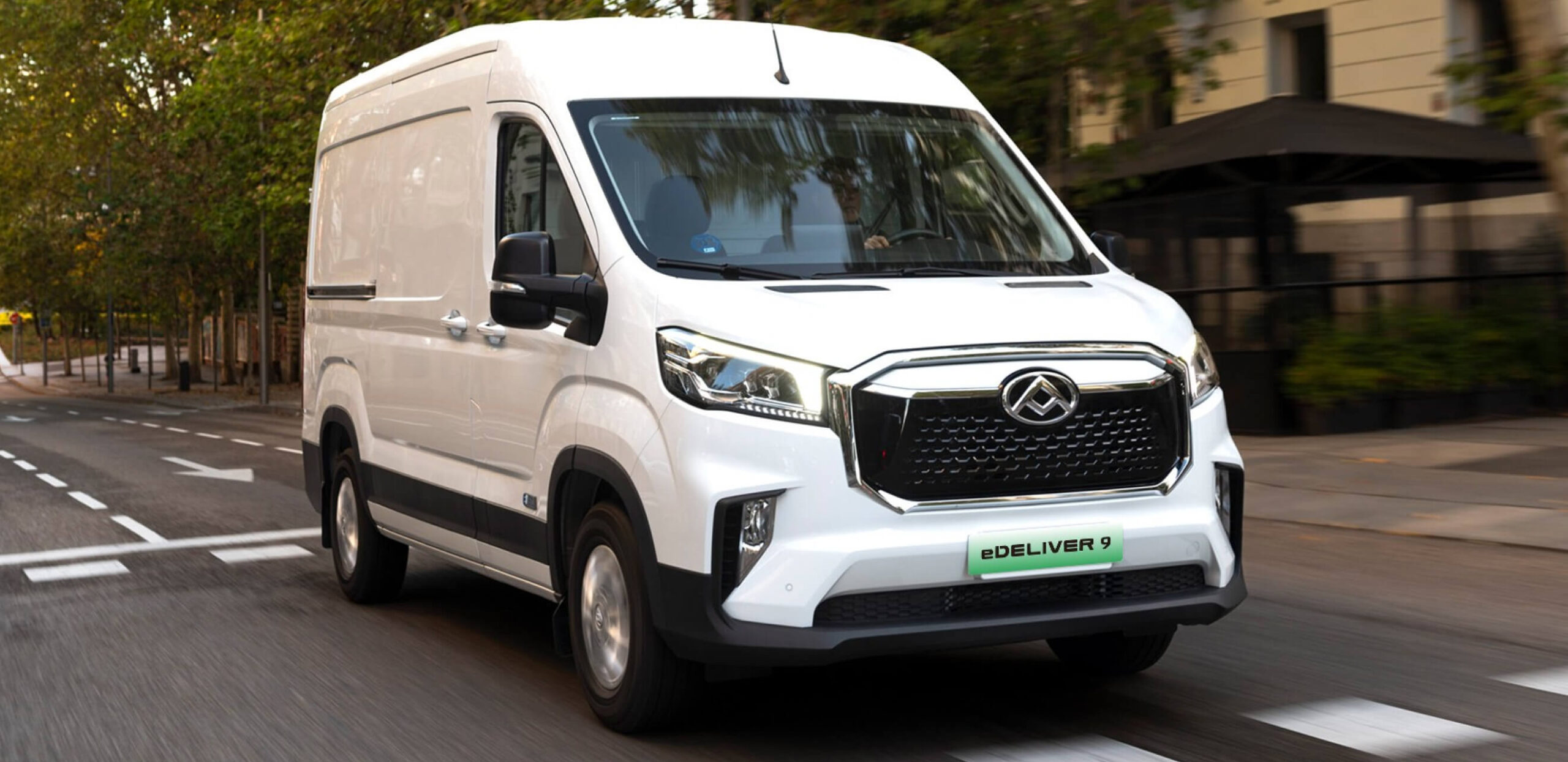 MAXUS eDELIVER 9 electric van in motion on a city street, featuring a modern front grille and aerodynamic design.