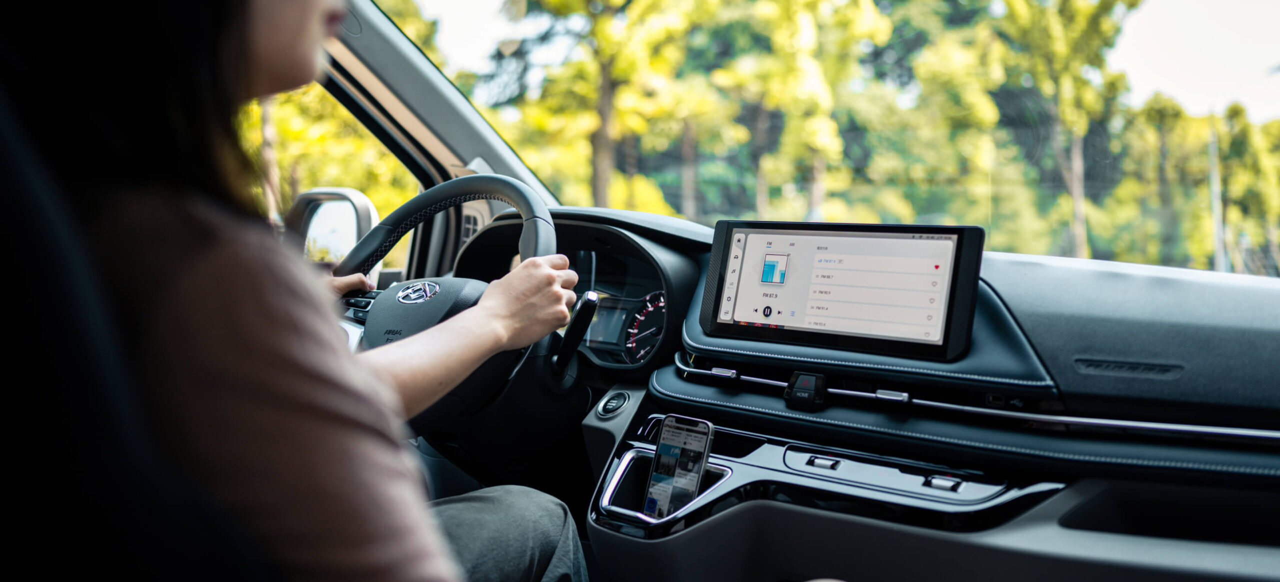 Interior view of a MAXUS electric vehicle, showing a driver using the advanced touchscreen infotainment system with a scenic outdoor background.